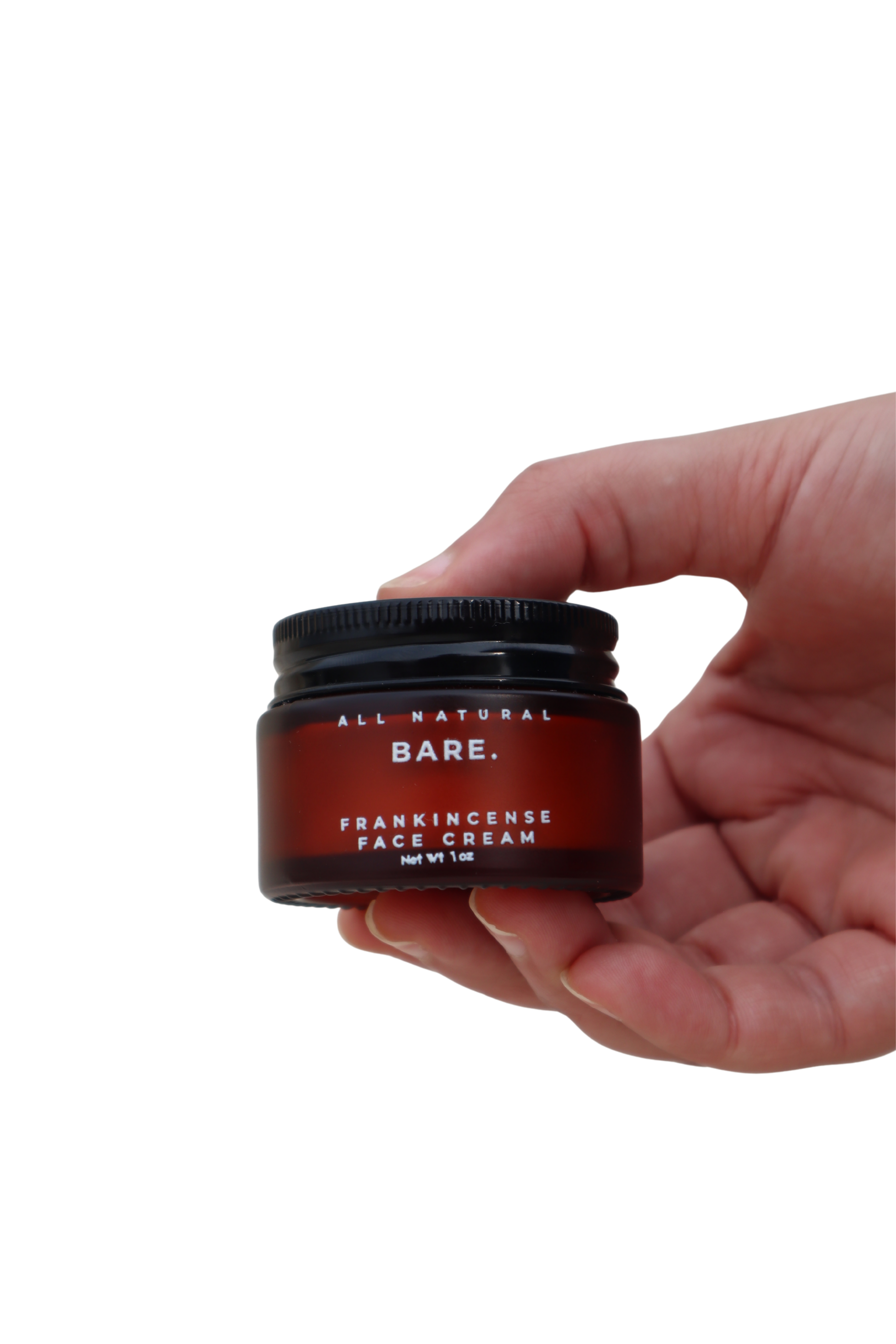 Hand holding a frosted amber glass jar of Bare Naturals Frankincense Face Cream on a clean white background