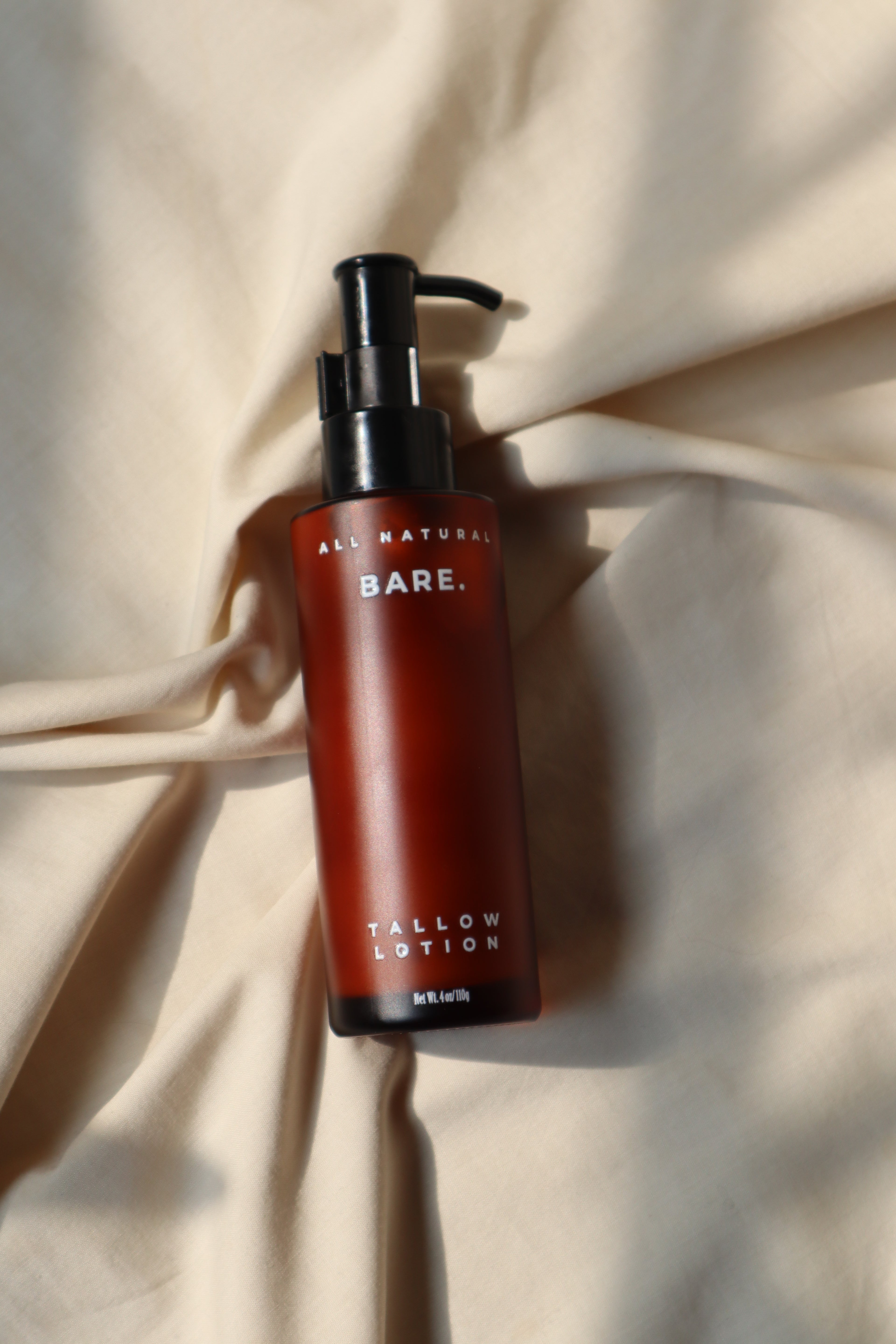 Red bottle, Bare Naturals Tallow Lotion with black pump on a beige fabric background