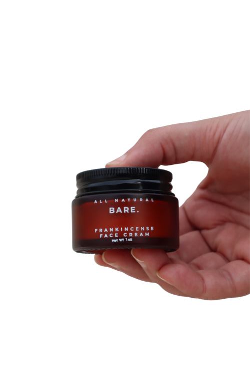 Hand holding a frosted amber glass jar of Bare Naturals Frankincense Face Cream on a clean white background, rich tallow face moisturizer for dry, normal and sensitive skin, non-comedogenic anti-aging skincare.