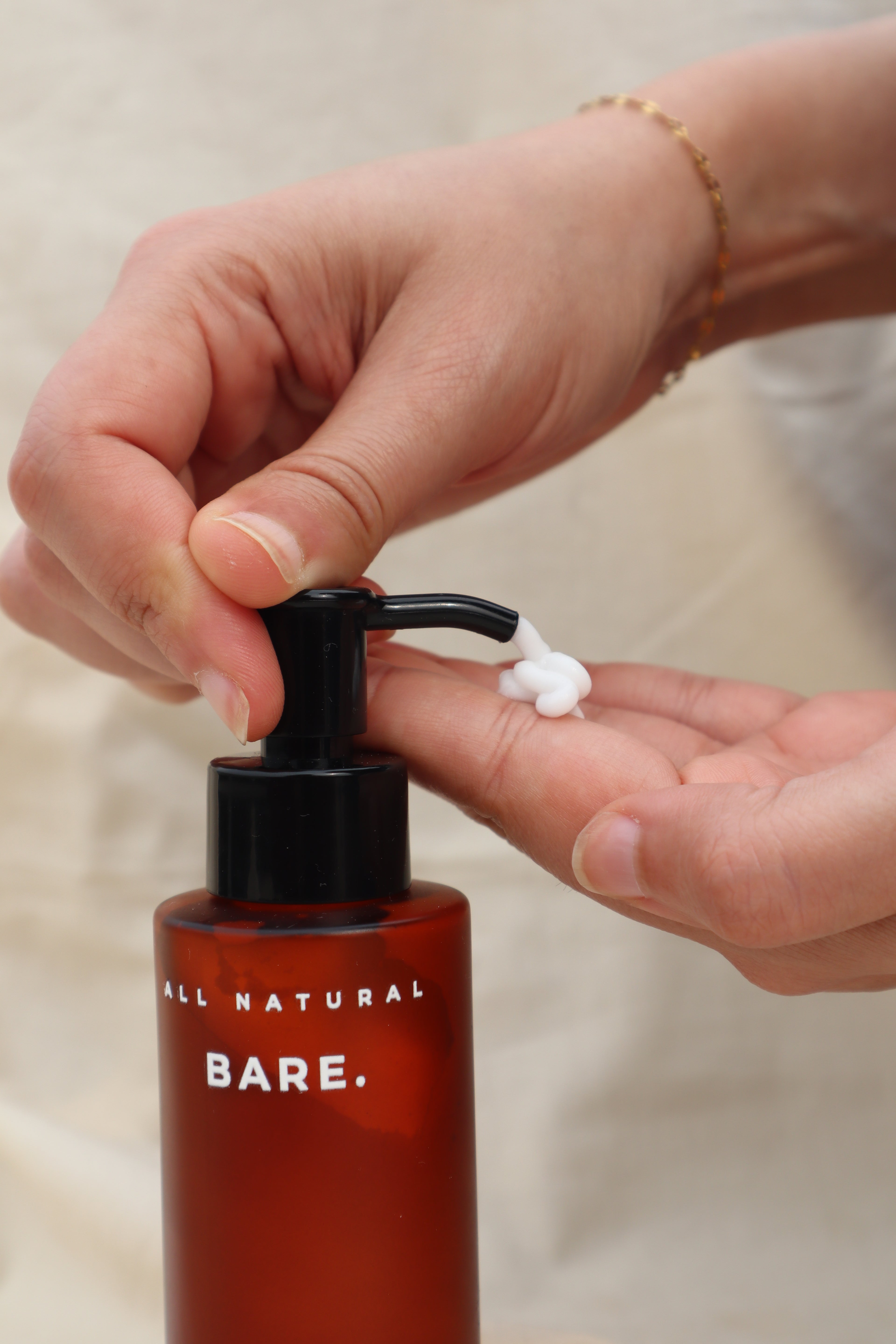 Person applying Bare Naturals Tallow Lotion from a frosted amber pump bottle onto their hand against a neutral background, lightweight daily moisturizer that supports the natural skin barrier and provides long-lasting hydration for dry, normal and sensitive skin.